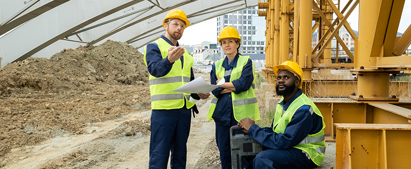 Gestão empresarial na construção civil: três operadores de obra conversam num canteiro de obras