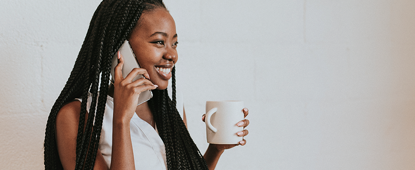 Indicação de clientes: mulher sorri ao telefone enquanto segura xícara de café