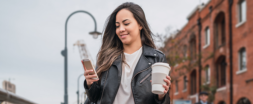 Leads: moça de jaqueta preta segura café e olha para o celular