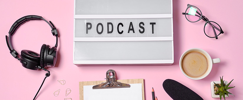 Venda 100% digital: um letreiro expõe a palavra "podcast" enquanto, ao redor, artigos de trabalho como prancheta, óculos, lápis, xícara e fone de ouvido repousam.