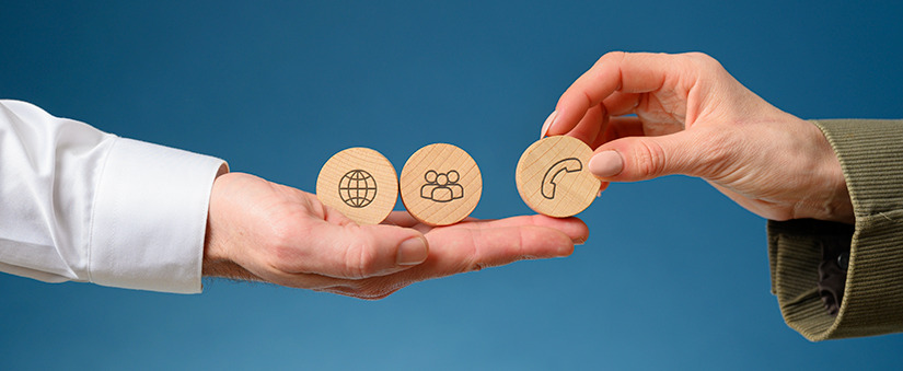 Suporte ao Cliente: mão posiciona três bolinhas de madeira com os ícones de mundo, pessoas e telefone noutra mão