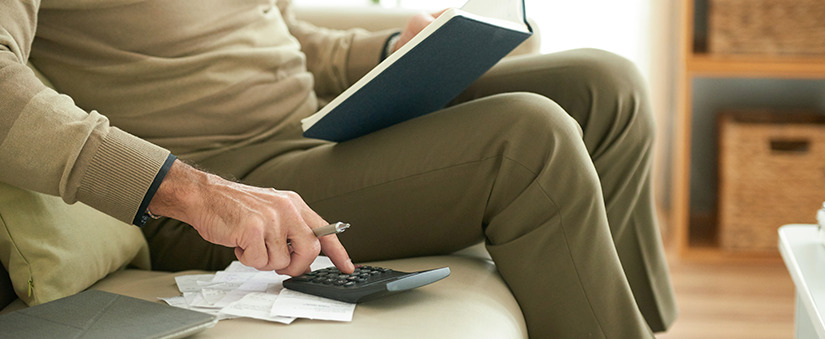 Análise de crédito: pessoa sentada no sofá usa calculadora realizando análise de crédito.