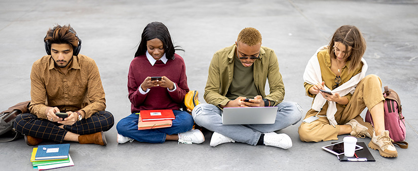 omnicanal: Estudantes com dispositivos digitais sentados no asfalto