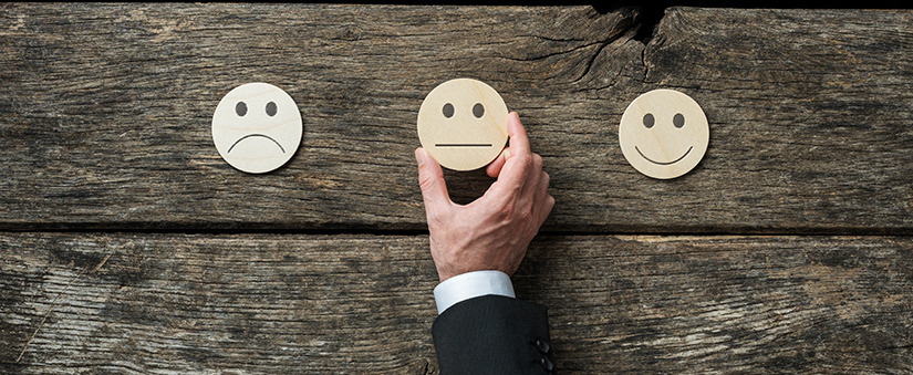 omnicanal: três emojis de madeira vistos de cima com expressões trsite, indiferente e feliz. 