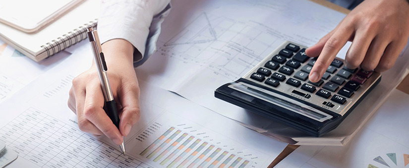 financiamento imobiliário: imagem de uma mesa com papeis e gráficos e as mãos de uma pessoa manuseando uma calculadora e uma caneta.