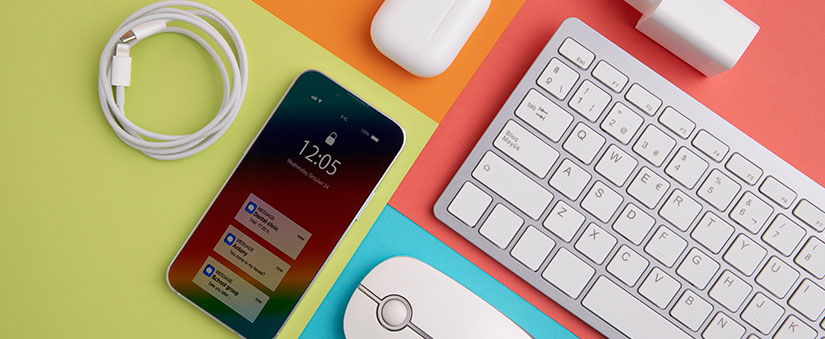 Ferramentas de Produtividade: imagem de uma mesa colorida, vista de cima, com alguns objetos em cima: celular, carregador, mouse, teclado, caixa de fones de ouvido.