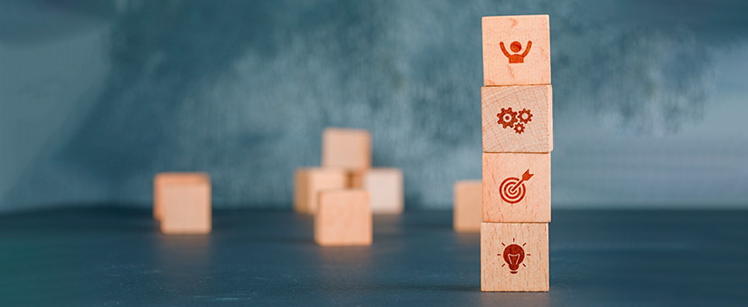 imagem de quatro cubos de madeira empilhados com ícones de uma pessoa, engrenagens, um alvo e uma lâmpada.