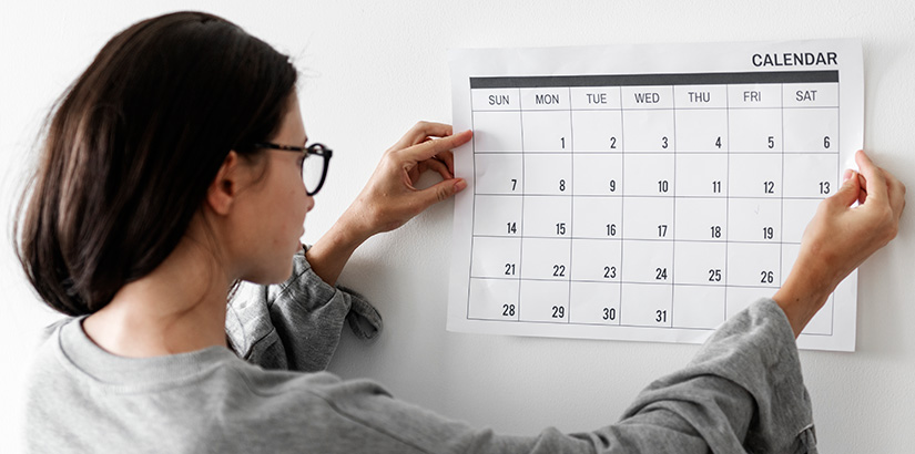 rotina imobiliária: mulher segurando um calendário na parede.