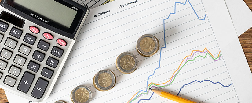 Taxas e impostos: imagem de uma mesa vista de cima com alguns papeis com gráficos, moedas empilhadas e uma calculadora.