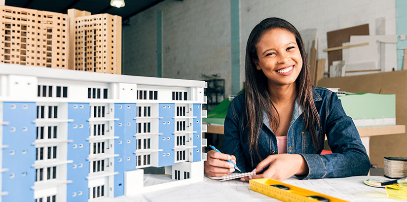 técnico em edificações: imagem de uma mulher sentada à frente de uma mesa com uma maquete de edifício.