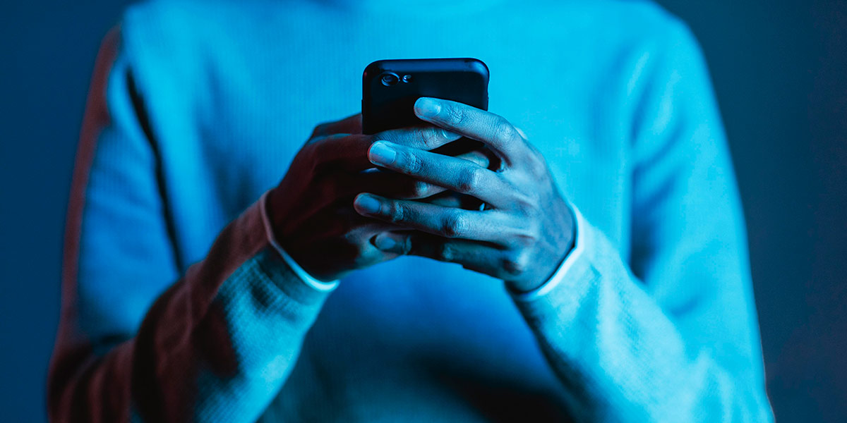 tecnologia persuasiva: close numa pessoa segurando um celular, destacada por uma luz azul.