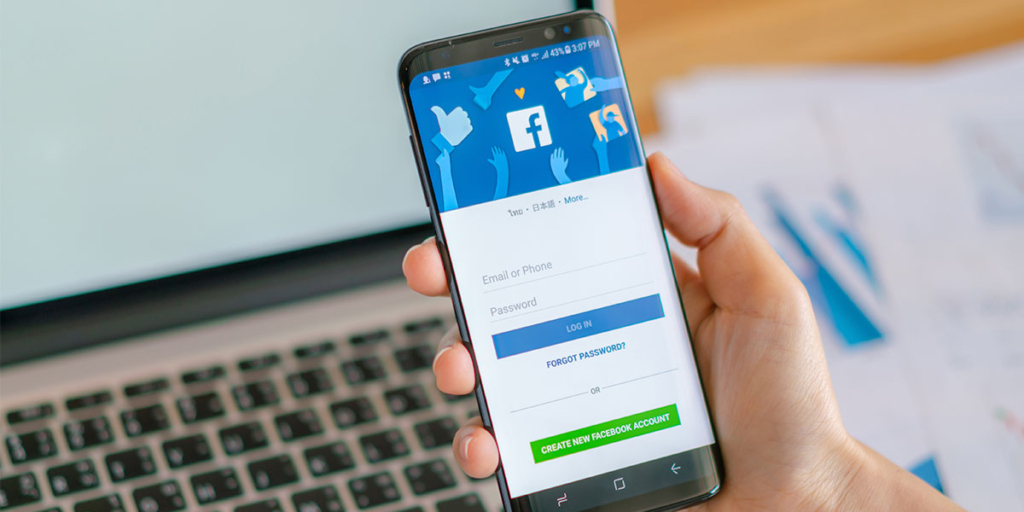 gerenciador de anúncio do facebook: close numa mão segurando um celular com a página de login do facebook aberta.