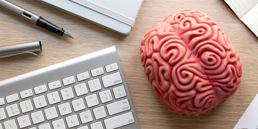 captar leads: imagem vista de cima de uma mesa com um teclado, alguns cadernos e canetas e a miniatura de um cérebro humano.