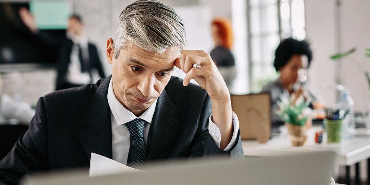 Burocracia Administrativa: homem usando terno, sentado à frente de uma mesa, com expressão de preocupação.