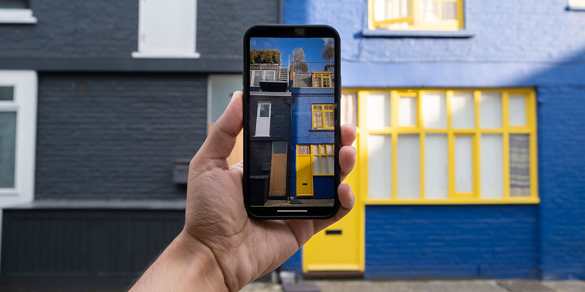 social mídia imobiliário: close numa mão segurando um celular apontando a câmera para um edifício à frente.