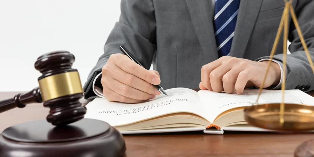 Mediação Imobiliária: imagem das mãos de um home de terno escrevendo num livro. À sua frente um malhete sobre a mesa.