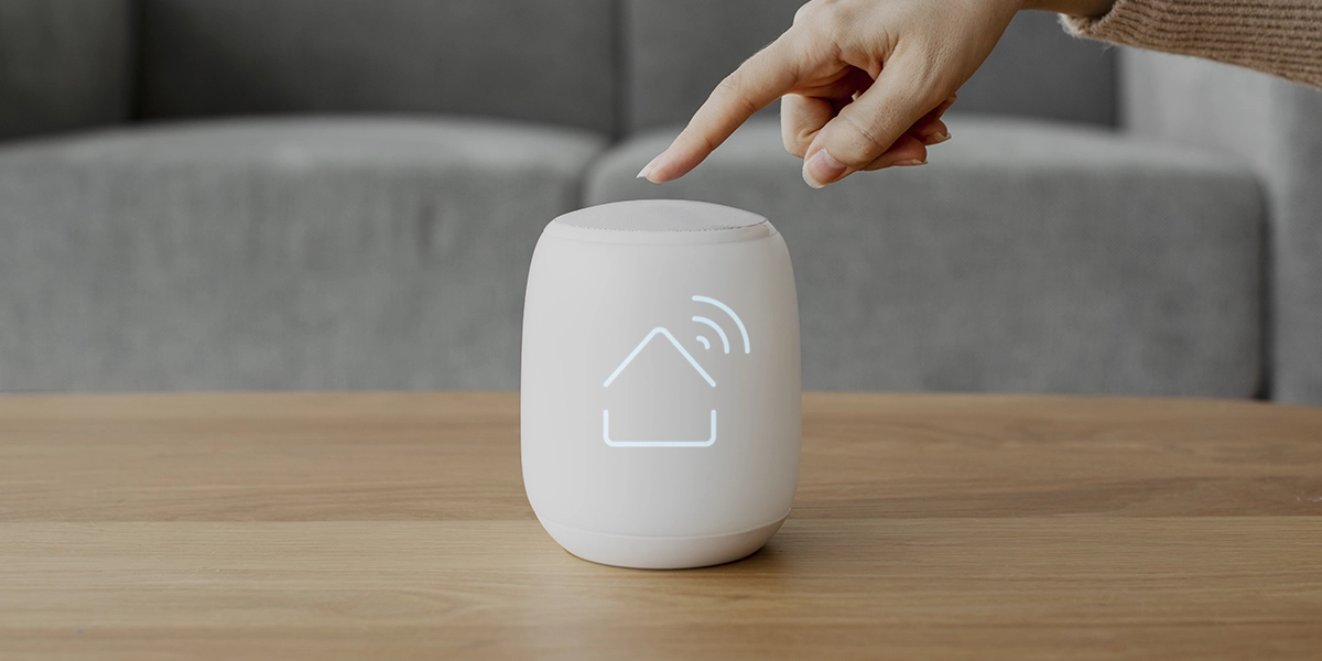 moradia inteligente: imagem de uma mão clicando num aparelho pequeno em cima de uma mesa, com o ícone de casa conectada no centro.