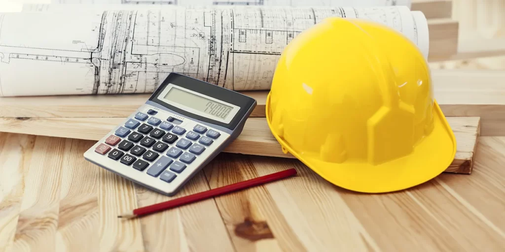 Como calcular custo de obra: imagem de uma mesa de madeira com alguns papeis com plantas de imóveis, um capacete de proteção e uma calculadora.