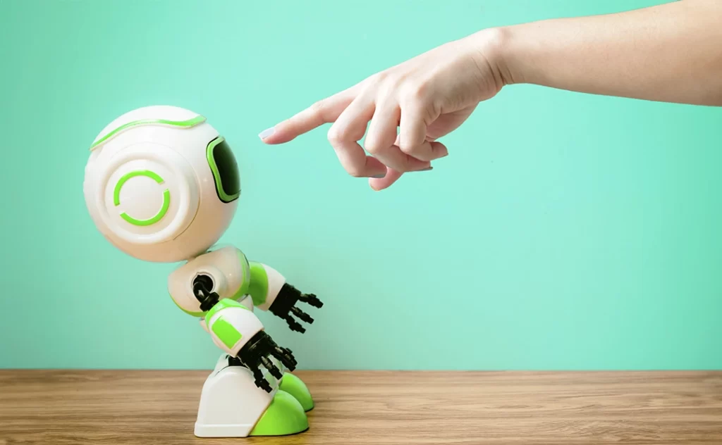 Inteligência artificial no mercado imobiliário: imagem de um pequeno robô e, ao seu lado, uma mão apontando o dedo para ele.