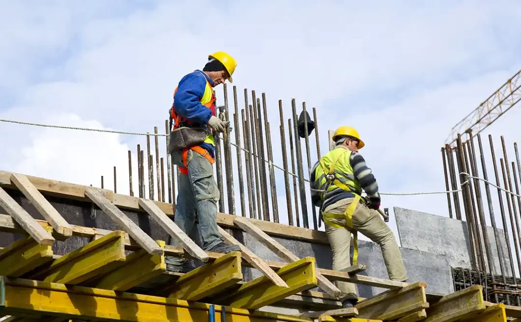 NR 17: imagem de um canteiro de obras e dois homens trabalhando numa estrutura alta.