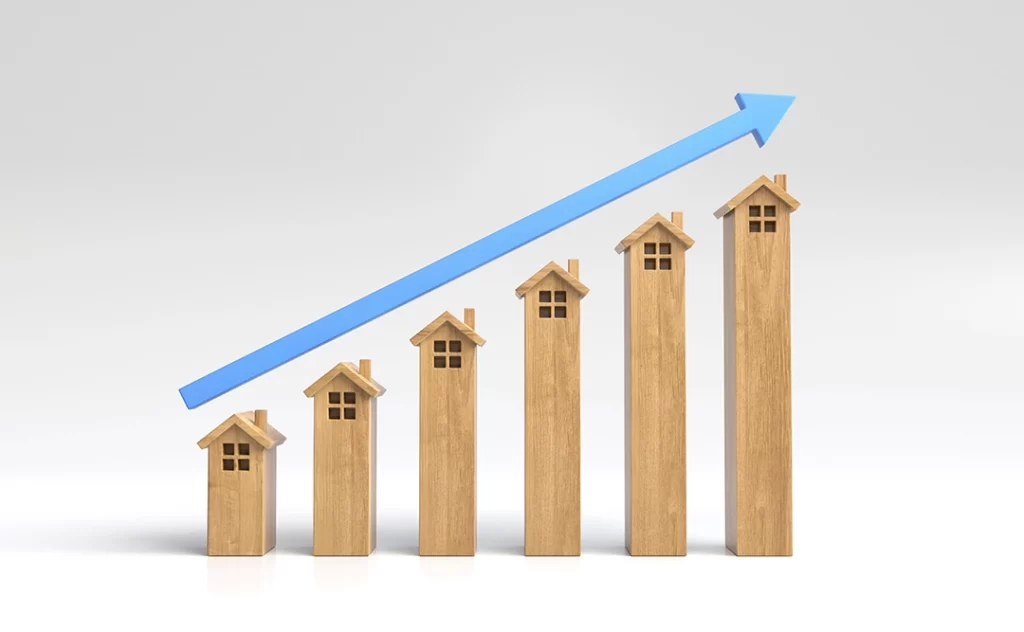 Indicadores imobiliários: A imagem mostra uma série de casas de madeira de diferentes alturas, dispostas em uma linha vertical, com a casa mais baixa no fundo e a mais alta no topo. Há uma seta azul apontando para cima, indicando um aumento ou crescimento.