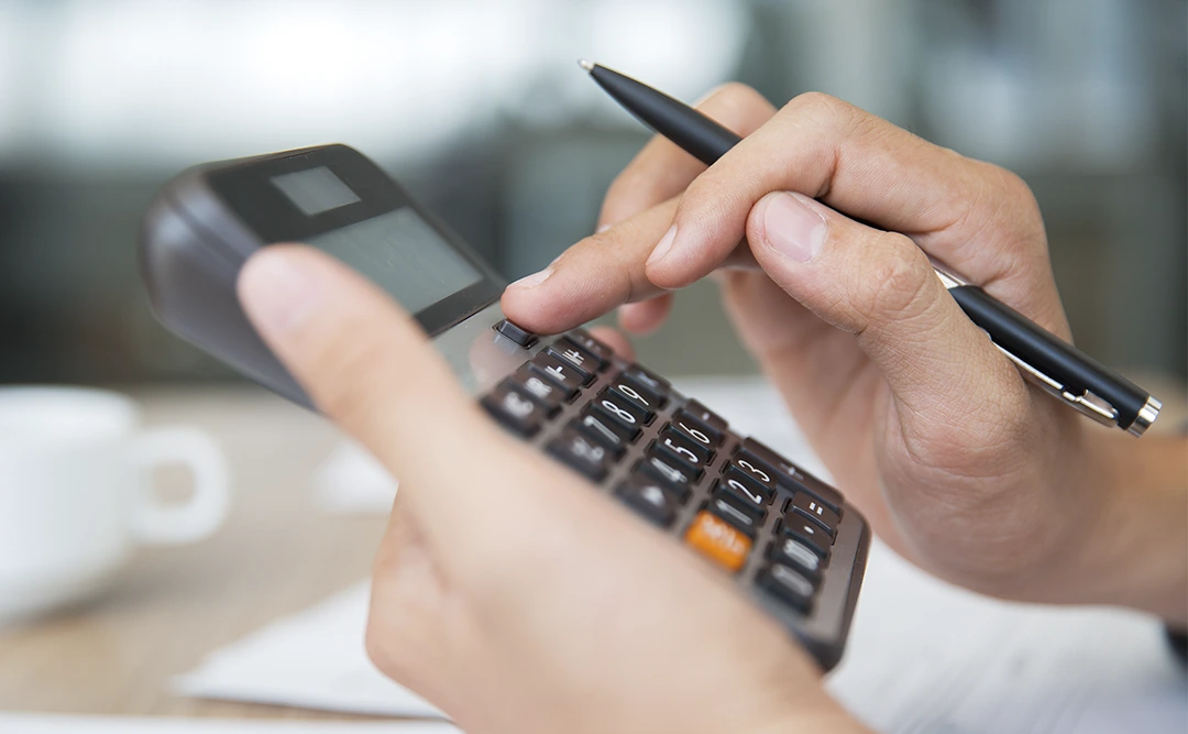 Regime especial de tributação para incorporadoras: close em mãos usando uma calculadora diante de uma mesa de escritório com alguns papeis.