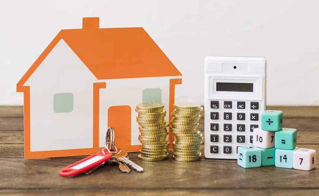 Regime especial de tributação para incorporadoras: a imagem mostra a ilustração de uma casa em miniatura em cima de uma mesa, com uma pilha de moedas ao lado. Vemos também uma calculadora e chaves em cima da mesa.