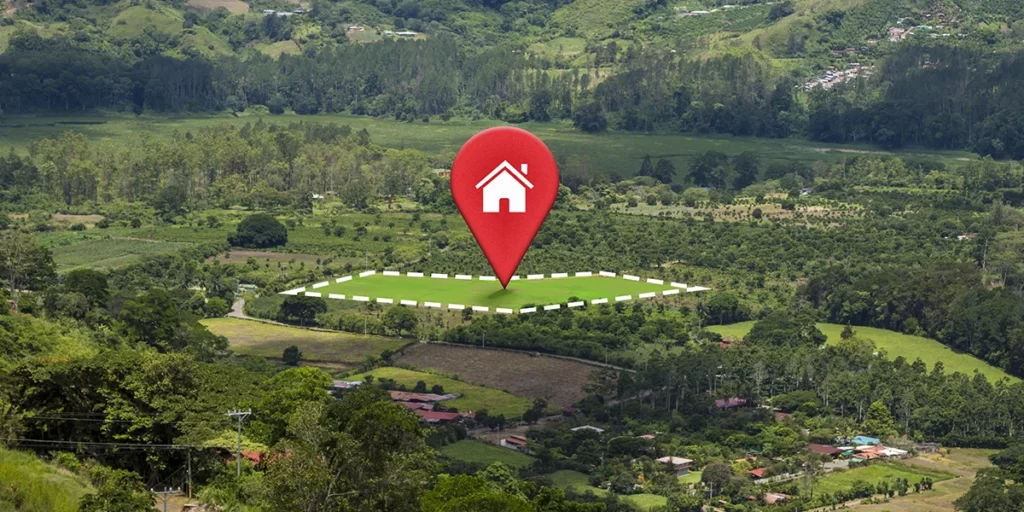 compra de lotes: A imagem mostra um mapa com um ponto vermelho indicando a localização de uma casa no meio de uma floresta verde com montanhas no fundo. A casa está rodeada por árvores e tem uma abóbora branca. O terreno ao redor é montanhoso e coberto por vegetação.
