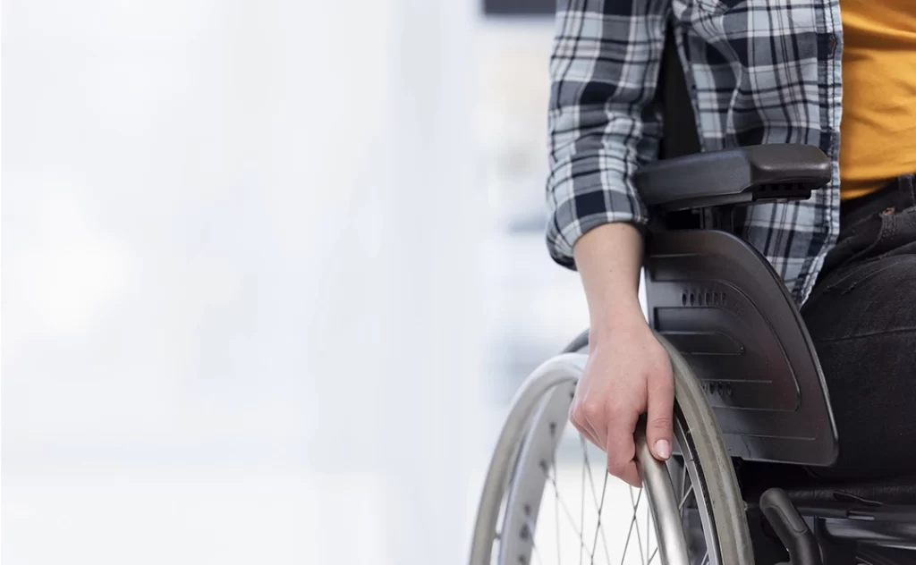 nbr 9050 atualizada: A imagem mostra o lado direito do corpo de uma pessoa em uma cadeira de rodas. A pessoa está usando uma camisa xadrez. O fundo é branco. 
