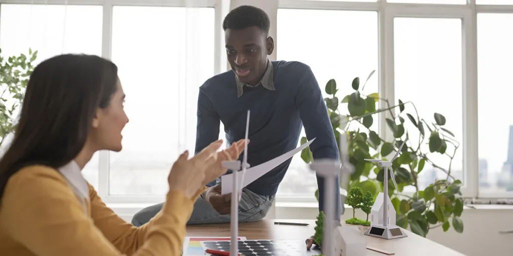 o que torna uma construção sustentável: imagem de duas pessoas conversando num escritório. Uma está sentada à frente de uma mesa e a outra está sentada na mesa.