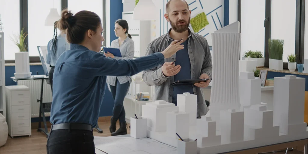  segmentação de clientes de construtoras: imagem de duas pessoas conversando e apontando para uma maquete de edifício. Os dois estão num amplo escritório. 