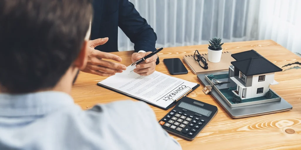 CRM para novos empreendimentos imobiliários: imagem de dois homens num escritório, de lados opostos de uma mesa de madeira. Um deles está de costas e conseguimos ver as mãos do segundo homem.