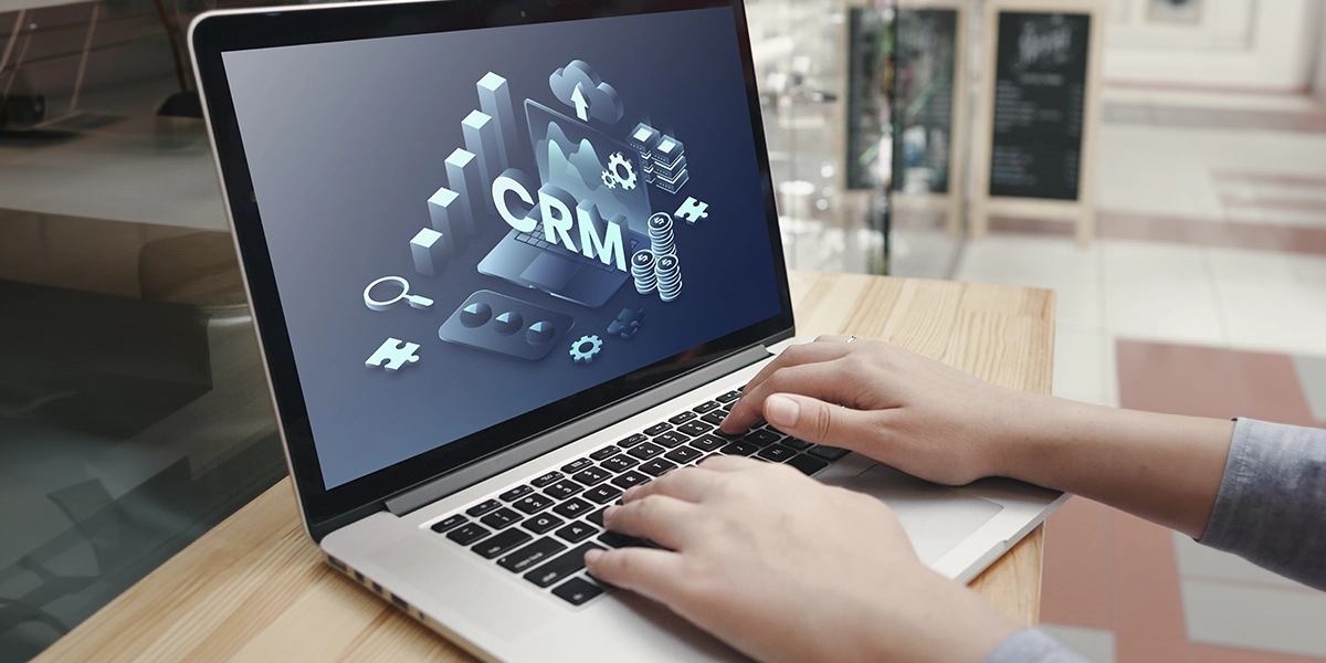 CRM para novos empreendimentos imobiliários: close em mãos digitando num teclado de notebook. Na tela uma ilustração com a sigla "CRM".