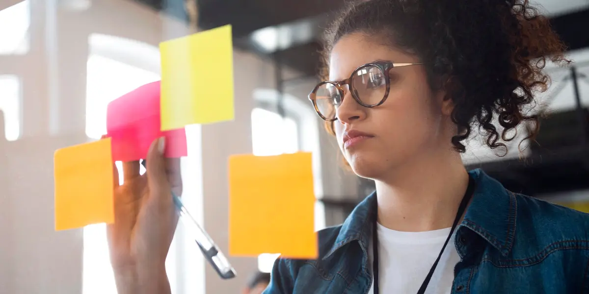 Gestão de Riscos para Incorporadoras: na foto, vemos uma mulher de cabelos cacheados e óculos, escrevendo em post-it coloridos