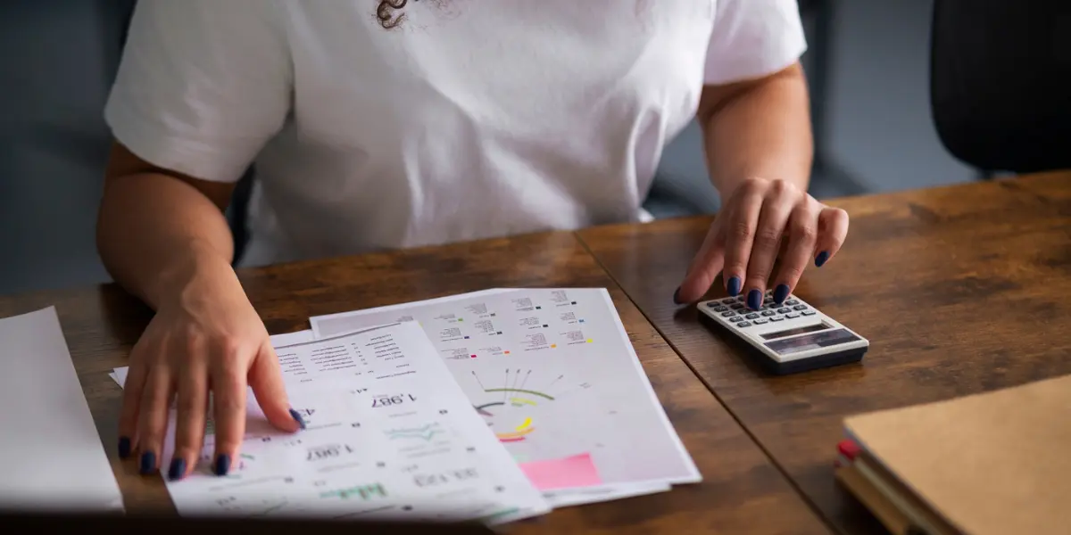 Relatórios de vendas de incorporadoras: a imagem apresenta uma mulher usando uma calculadora enquanto observa uma folha com números