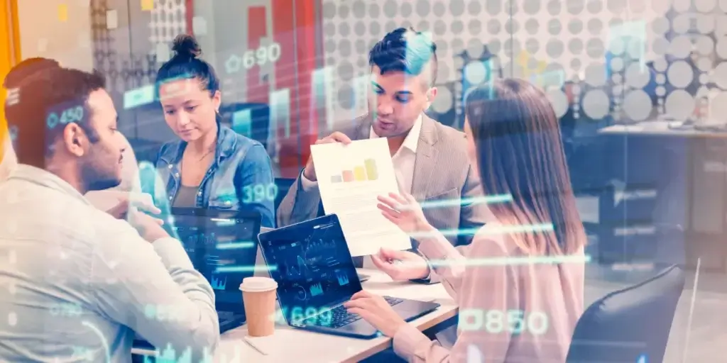 vender com CRM vender com CRM: imagem de uma reunião de negócios num escritório. Várias pessoas estão em volta de uma mesa olhando gráficos em papéis e notebooks.
