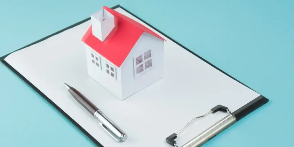 Matrícula do imóvel Matrícula do imóvel: imagem mostra uma miniatura de uma casa em cima de uma prancheta, com uma folha de papel presa nela. Há uma caneta ao lado.