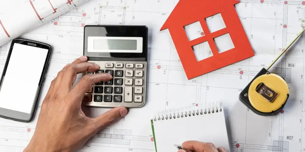 Fornecedores para construtoras Fornecedores para construtoras: imagem mostra mãos vista de cima com artigos de papelaria, uma calculadora, uma trena, um bloquinho e um celular.