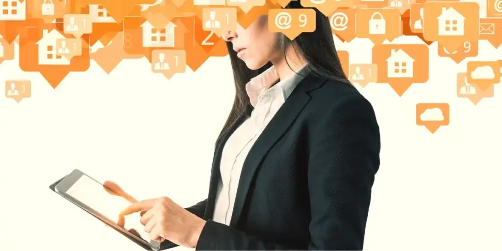 follow up imobiliário: A composição da cena mostra uma mulher parcialmente visível, posicionada no lado esquerdo da imagem, inclinada para a direita enquanto manipula um tablet. cima dela, em um fundo branco, flutuam vários ícones laranjas em forma de balões de fala, cada um contendo representações gráficas como casas, figuras de pessoas, símbolos de e-mail e cadeados, que sugerem notificações e atividades online.