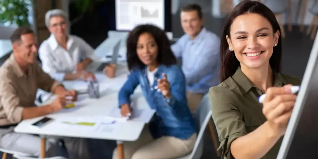 Treinamento de corretores: imagem mostra um grupo de quatro pessoas, sendo três homens e uma mulher, sentados em uma mesa retangular. Na frente deles há uma mulher em pé, escrevendo em uma espécie de quadro, aparentando ser uma demonstração. 