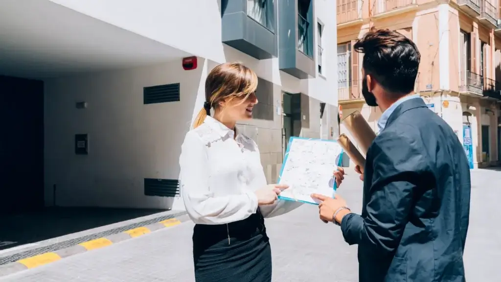 CRM Imobiliário: A cena se passa em uma rua estreita entre edifícios altos. A composição é dividida verticalmente, com o homem à direita e a mulher à esquerda, ambos voltados um para o outro, segurando e apontando para um mapa. 