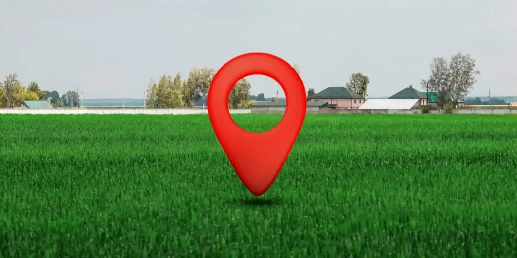 Como vender lotes encalhados: imagem mostra um terrenos com uma grama verde e um ícone gigante de localização no meio do terreno. Ao fundo da imagem há casas e árvores.