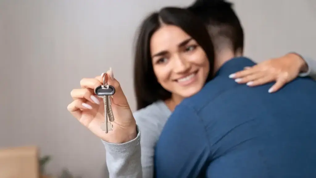 lead scoring imobiliário lead scoring imobiliário: imagem mostra um homem e uma mulher se abraçando. Ela está de frente para a imagem e segura uma chave com uma das mãos.